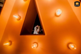 The bride and groom share a kiss, creatively framed through a glowing triangular marquee letter during their wedding in Cancun, Mexico